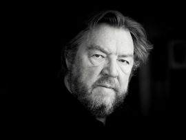 Schwarz-Weiß-Porträt des Bassbaritons Robert Holl. Mit ernstem Blick schaut er leicht an der Kamera vorbei, während sein Gesicht durch weiches Seitenlicht hervorgehoben wird.