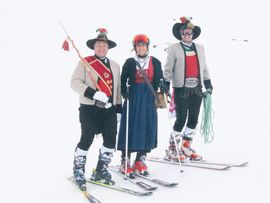 drei Menschen im Schnee mit Trachten und Skiern