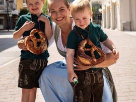 zwei Kinder mit Brezen um ihren Hals posieren für ein Foto mit ihrer Mutter