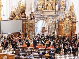 Ein Orchester spielt vor Publikum in einer prachtvoll barock ausgestatteten Kirche.