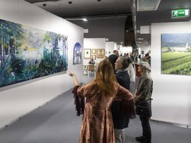 Besucher:innen betrachten großformatige Kunstwerke in einer Ausstellungshalle.
