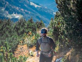 Ein Trailrunner läuft auf einem schmalen alpinen Wanderweg zwischen Latschenkiefern und felsigem Gelände.