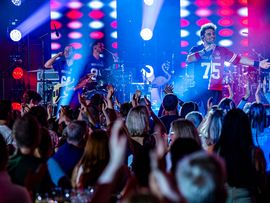 Konzertband tritt vor Publikum auf einer beleuchteten Bühne mit farbiger Lichtshow auf.