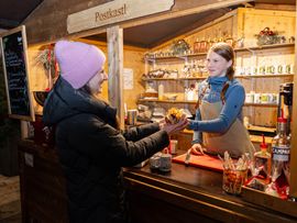 Eine lachende Frau kauft etwas bei einem Weihnachtsmarktstand