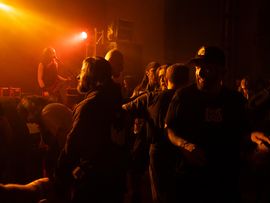 Publikum vor einer Bühne bei einem Konzert, beleuchtet von orangefarbenem Scheinwerferlicht.