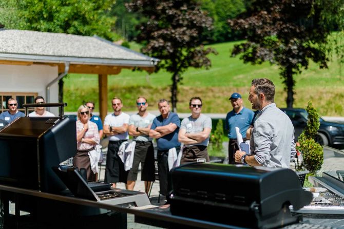 Helmut Hochfilzer erklärt etwas vor dem Grill während einige Personen im zuhören