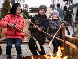 3 Kinder braten Würstel am Feuer beim Adventsmarkt