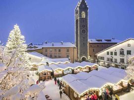 Weihnachtsmarkt in Sterzing mit hell erleuchtetem Weihnachtsbaum und Hütten.