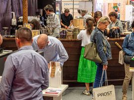 Besucherinnen und Besucher an einem Gastronomie- und Kaffeestand auf einer Messe mit Kaffeemaschinen, Produkten und Verkaufstresen.