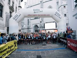 Läuferinnen und Läufer stehen unter einem großen Startbogen in einer Altstadt und warten auf den Beginn eines Trailruns.