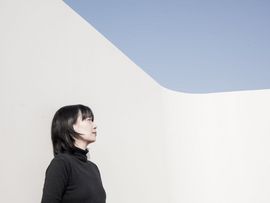 ©PaikDahuim Porträt der Autorin Kang Han im Profil vor einer hellen, minimalistischen Architektur mit blauem Himmel.