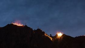 Leuchtende Feuer entlang eines Berggrats bei Nacht vor bewölktem Himmel.