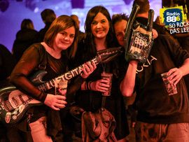 Drei Besucher posieren gut gelaunt mit einer E-Gitarre und einem Rock-Accessoire.