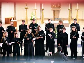 Tiroler Landesjugendchor bei einem Konzertauftritt in einem festlich gestalteten Saal. Die Sängerinnen und Sänger stehen in zwei Reihen und halten Notenmappen, während sie gemeinsam musizieren.