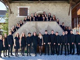 Gruppe des Tiroler Landesjugendchors vor einem historischen Gebäude. Die Sängerinnen und Sänger stehen gemeinsam für ein Gruppenfoto vor einer steinernen Fassade und tragen überwiegend schwarze Kleidung.