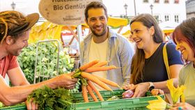 Auf einem Wochenmarkt verkauft ein Verkäufer Möhrchen an Kunden