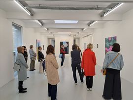 mehrere Menschen betrachten Kunst in einem weißen Gang