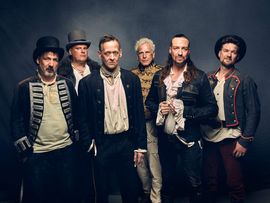 ©Robert Eikelpoth Die sechs Mitglieder von In Extremo posieren in historischen Bühnenkostümen vor einem dunklen Hintergrund. Das Gruppenporträt vermittelt den markanten Mittelalter-Rock-Stil der Band.