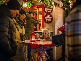 Familie steht auf dem Imster Adventsmarkt um einen Tisch mit Kerze herum und unterhält sich.