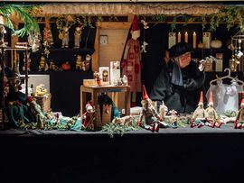 Marktstand mit handgefertigten Wichtelfiguren, Stofftieren und weihnachtlichen Dekorationsartikeln bei stimmungsvoller Beleuchtung.