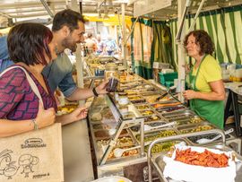 Auf einem Wochenmarkt verkauft eine Verkäuferin Essen an Kunden