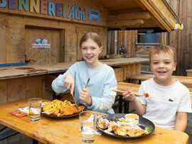 Zwei Kinder essen in der Erlebnis Sennerei Zillertal Schnitzel mit Pommes und Kaiserschmarrn.