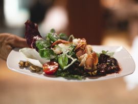 Servierter Blattsalat mit Trauben, Nüssen und Speck auf einem Teller.
