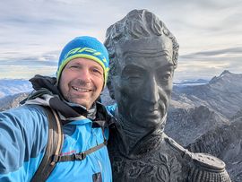 Bergsteiger vor Statue mit Bergen im Hintergrund