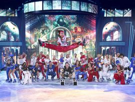 Eisläufer auf einer Bühne schauen einem anderen Eisläufer zu, wie er einen Sprung macht