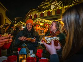 Eine Gruppe von Freunden steht mit dampfenden Tassen Glühwein im Kreis und unterhält sich.