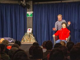 Markus Koschuh tritt auf einer Bühne auf mit einer Puppe