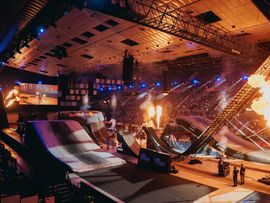 Blick über die Masters-of-Dirt-Arena mit großen Sprungrampen, Spezialeffekten und Flammen. Die Zuschauertribünen sind bis auf wenige Plätze gefüllt.