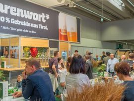 Messehalle mit Messeständen, vor denen viele Besucher:innen stehen und sich verschiedene Biersorten anschauen.