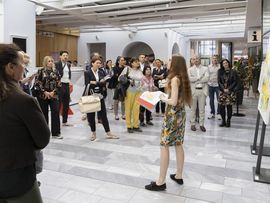 Menschen stehen in einem Lichthof um eine Frau, die etwas präsentiert