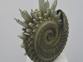 Skulptur einer spiralförmigen Schneckenmuschel, aus deren Rand zahlreiche kleine Hochhäuser herausragen.