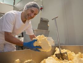 Mitarbeiter der Erlebnis Sennerei verarbeitet in der Produktion eine große Menge Milchprodukt.