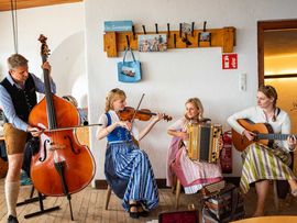 Vier Musiker:innen spielen in Tracht in einem gemütlichen Gastraum.