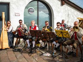 Volksmusikgruppe spielt vor einem Gebäude mit Blick auf die Tiroler Berglandschaft.