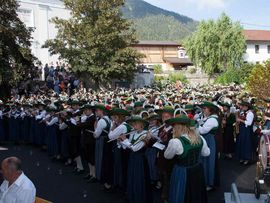 ©Ludwig Auer Hunderte Musikantinnen und Musikanten in Tracht spielen gemeinsam bei einem großen Freiluftkonzert vor der Kirche in Sautens.
