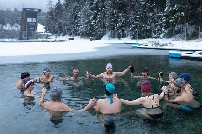 Eisbadende im See im Kreis stehend vor Winterkulisse