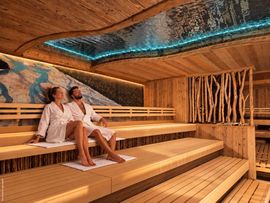 Großzügige Holzsauna mit zwei entspannten Personen in Bademänteln.