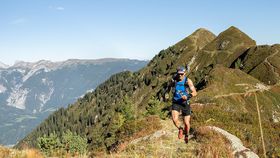 Ein Trailrunner läuft auf einem schmalen Berggrat mit weiter Aussicht auf alpine Gipfel und Täler.