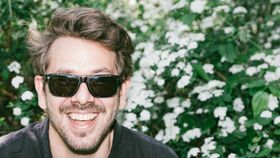 Mann lacht vor Gebüsch in die Kamera