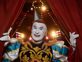 Circus Roncalli Clown lächelt durch roten Vorhang in die Kamera