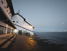 Terrasse der Nordkettenbahn mit Holzbänken und Blick auf die verschneite Bergkulisse in der Abenddämmerung.