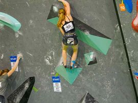 Eine Frau, die eine Kletterwand erklimmt in der Alpinmesse erklimmt.
