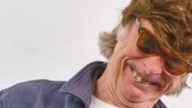 Mann grinst mit Sonnenbrille und Perücke in die Kamera