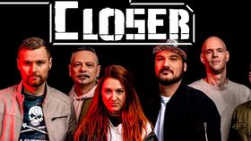 Bandfoto vor schwarzem Hintergrund: sieben Personen stehen nebeneinander, mittig eine Frau mit orangen Haaren, darüber der Schriftzug „One Step Closer“.