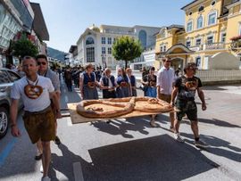 Menschen mit Brezen um den Hals tragen eine große Breze