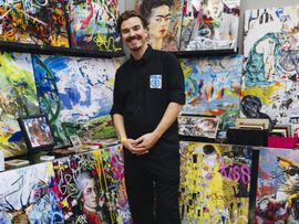 Mann posiert vor bunten abstrakten Gemälden